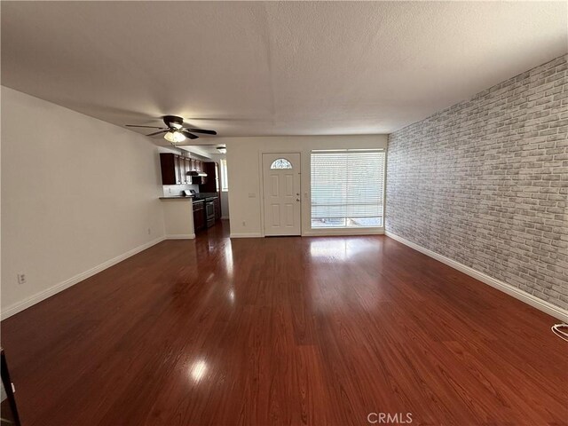 unfurnished living room with a ceiling fan, baseboards, dark wood-style flooring, and a textured ceiling