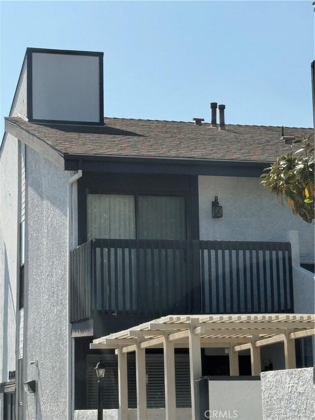 view of exterior entry with roof with shingles, stucco siding, and a balcony