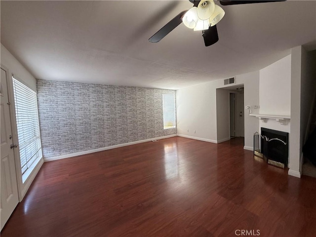 unfurnished living room with baseboards, a ceiling fan, a fireplace, and dark wood-type flooring
