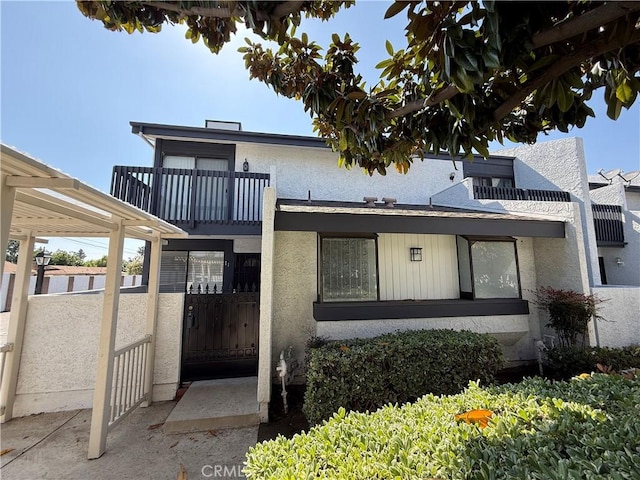 view of front of property featuring stucco siding, a gate, fence, and a balcony