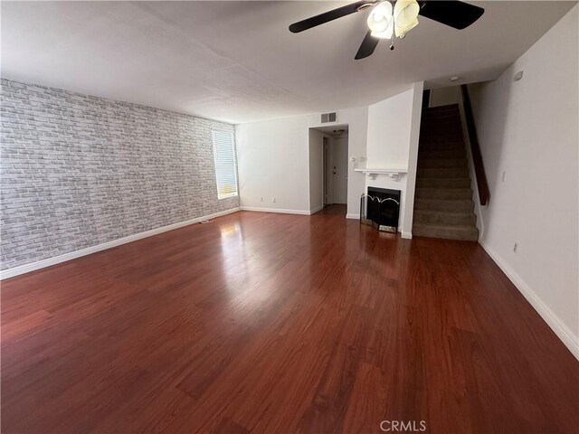 unfurnished living room with a ceiling fan, baseboards, stairway, wood finished floors, and brick wall