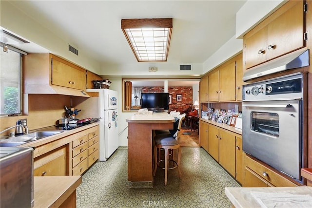 kitchen featuring oven, light countertops, freestanding refrigerator, under cabinet range hood, and a breakfast bar