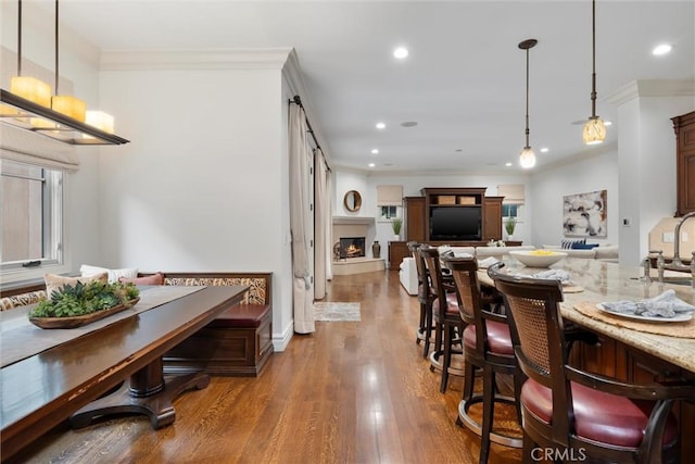 dining space with crown molding, wood finished floors, a lit fireplace, and recessed lighting