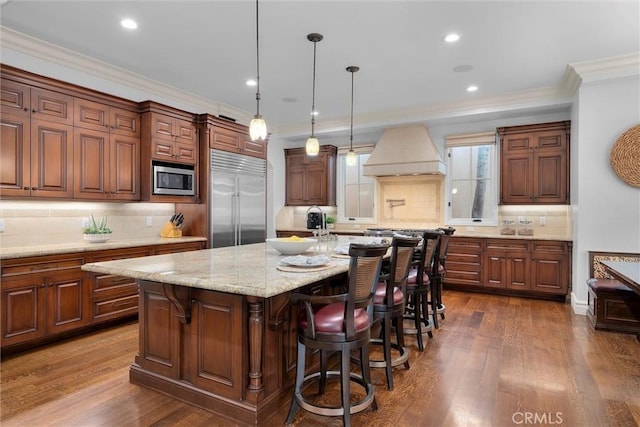 kitchen with built in appliances, premium range hood, ornamental molding, backsplash, and a kitchen island