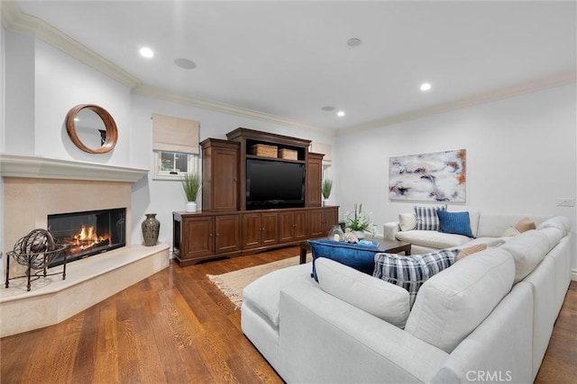 living area featuring crown molding, wood finished floors, a glass covered fireplace, and recessed lighting