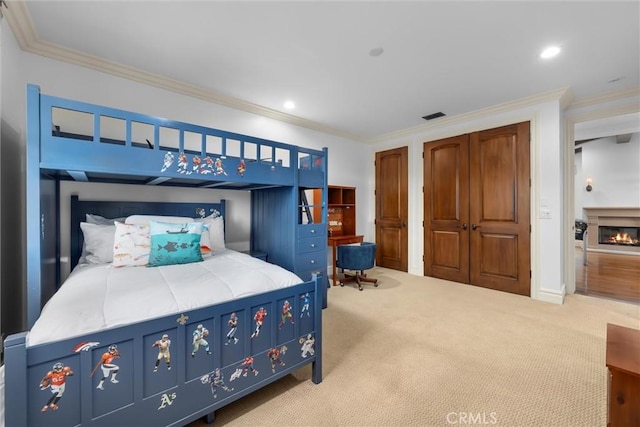bedroom featuring carpet floors, ornamental molding, a glass covered fireplace, recessed lighting, and multiple closets