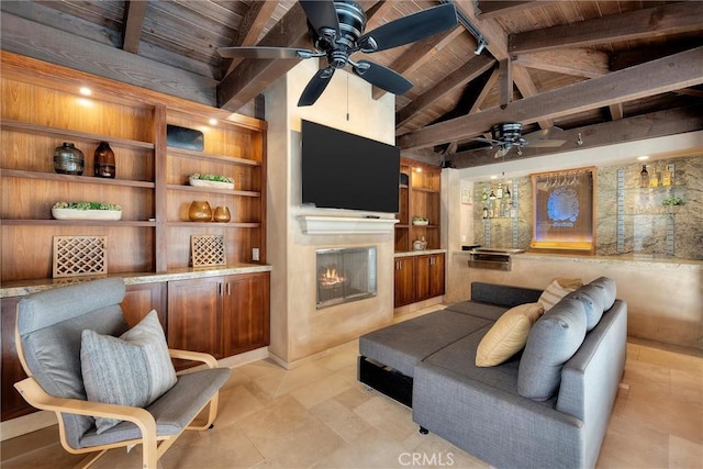 living room with a ceiling fan, wooden ceiling, a glass covered fireplace, beamed ceiling, and built in shelves