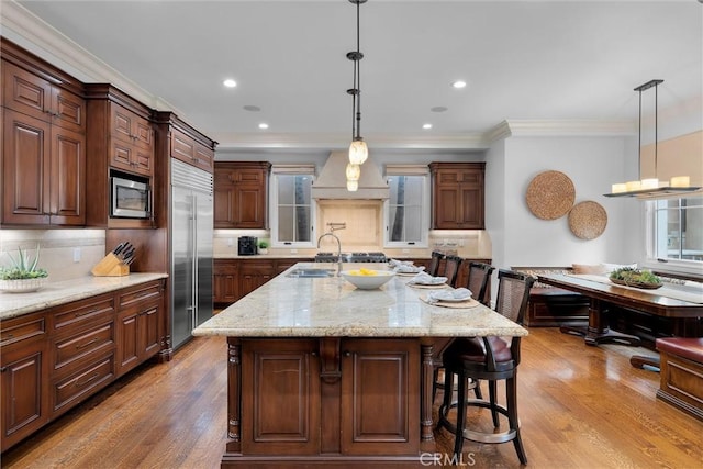kitchen with built in appliances, wood finished floors, backsplash, a breakfast bar, and crown molding