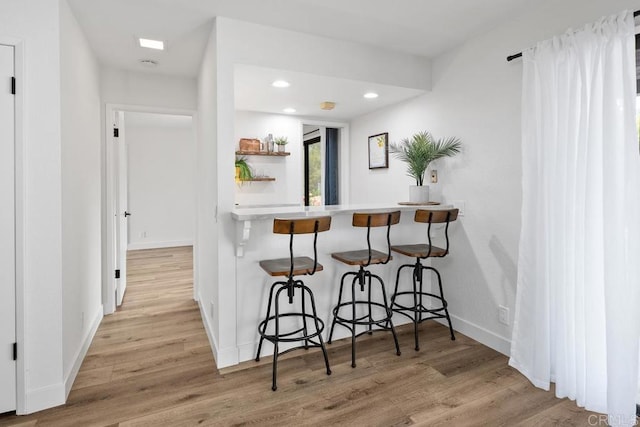 kitchen with baseboards, a breakfast bar, recessed lighting, and wood finished floors