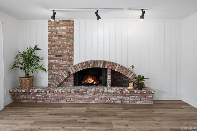 room details with rail lighting, a brick fireplace, baseboards, and wood finished floors