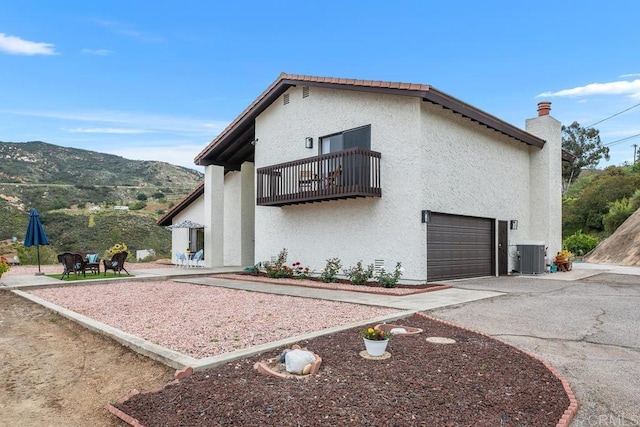 exterior space featuring a mountain view, stucco siding, central AC unit, a balcony, and driveway