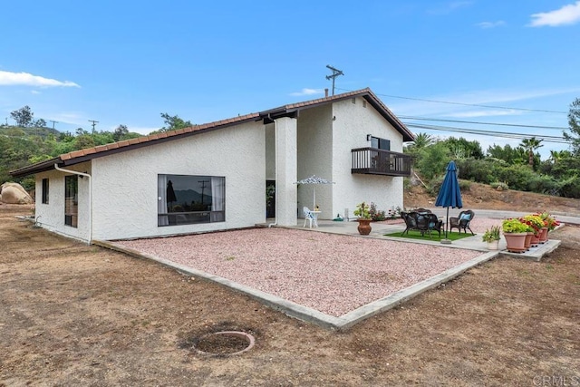 rear view of property with a patio, stucco siding, a fire pit, and a balcony