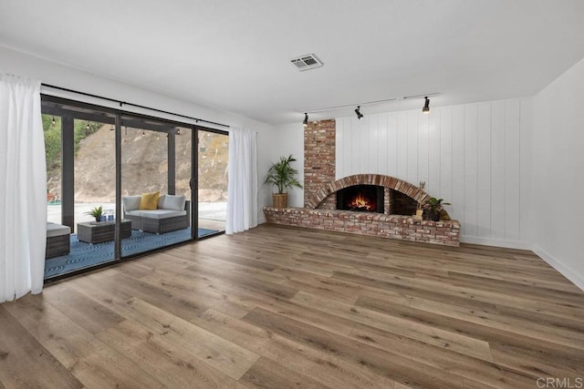 unfurnished living room with a brick fireplace, visible vents, track lighting, and wood finished floors