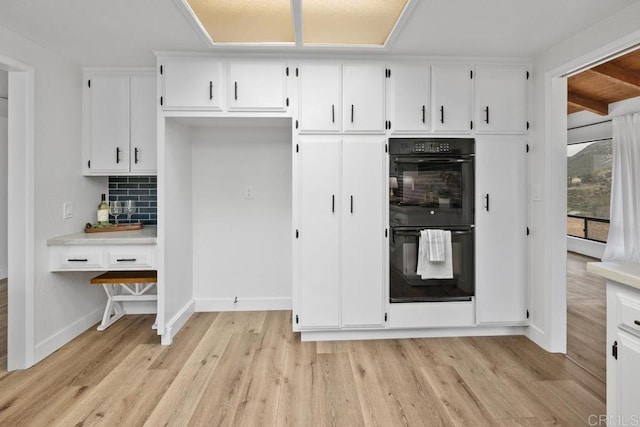 kitchen featuring light wood-type flooring, decorative backsplash, white cabinets, dobule oven black, and baseboards
