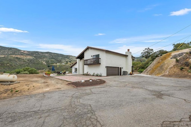 view of side of home with a mountain view, stucco siding, a chimney, a balcony, and driveway
