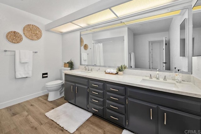 bathroom featuring toilet, wood finished floors, baseboards, and a sink