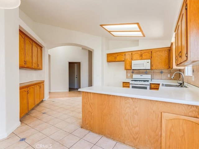 kitchen featuring white appliances, a sink, a peninsula, arched walkways, and light countertops