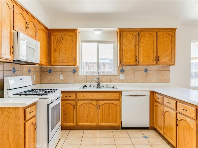 kitchen featuring a sink, tasteful backsplash, white appliances, brown cabinets, and light countertops