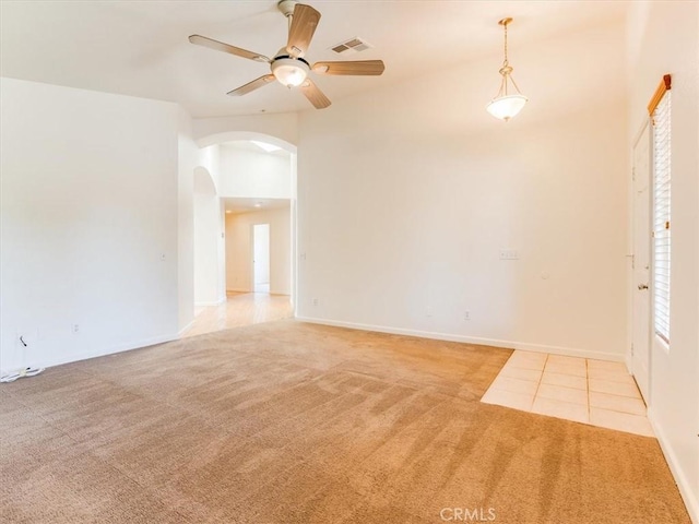 carpeted spare room featuring a ceiling fan, visible vents, tile patterned flooring, baseboards, and arched walkways