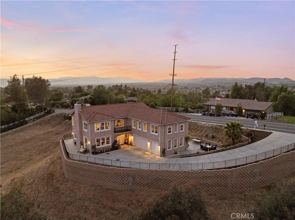 back of property at dusk featuring a garage, concrete driveway, a chimney, a fenced backyard, and a tile roof