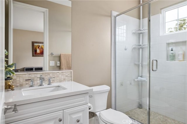 bathroom with a shower stall, toilet, vanity, and backsplash