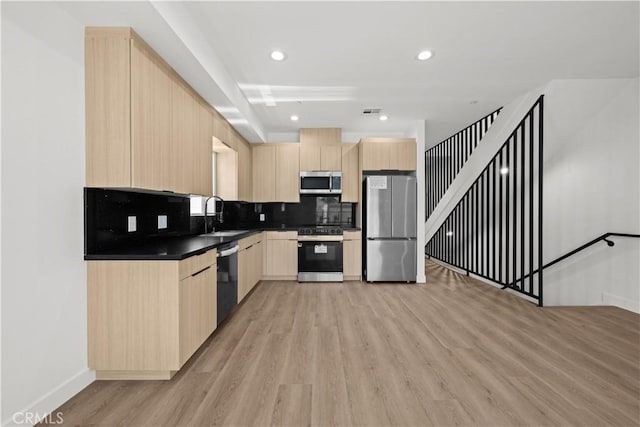 kitchen with light brown cabinets, light wood-style flooring, a sink, dark countertops, and stainless steel appliances