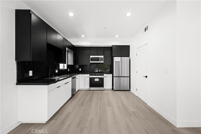 kitchen with light wood-style flooring, dark cabinets, a sink, dark countertops, and stainless steel appliances