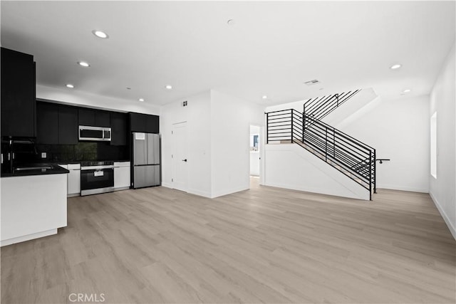 kitchen with dark cabinets, light wood-style flooring, a sink, stainless steel appliances, and recessed lighting