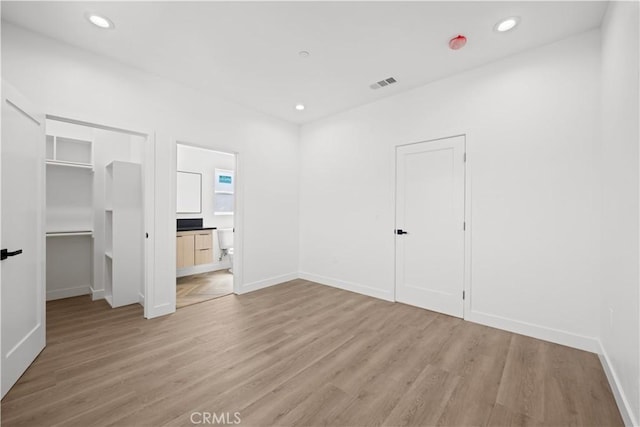 unfurnished bedroom featuring light wood finished floors, a walk in closet, baseboards, and visible vents