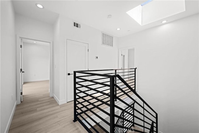 corridor featuring an upstairs landing, light wood-style flooring, visible vents, and a skylight