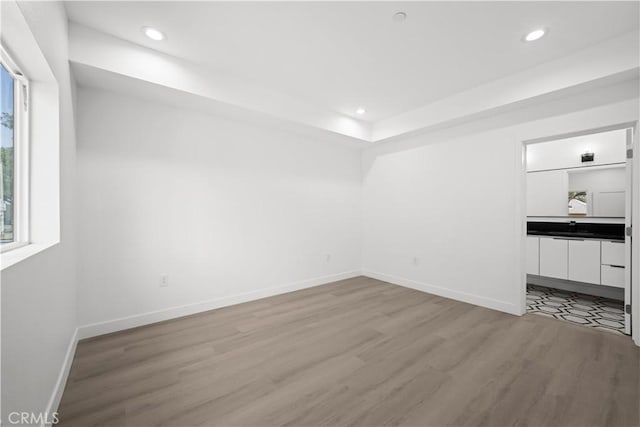 interior space with light wood finished floors, a raised ceiling, baseboards, and recessed lighting