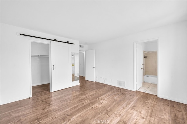 unfurnished bedroom with light wood-style flooring, a barn door, baseboards, and a closet