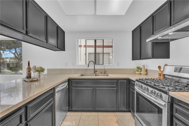 kitchen with stainless steel appliances, a sink, light tile patterned flooring, wall chimney range hood, and light stone counters