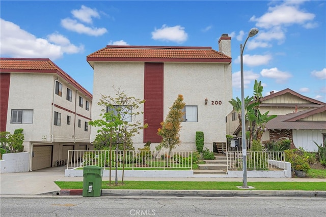view of front facade with stucco siding, concrete driveway, a chimney, an attached garage, and a fenced front yard