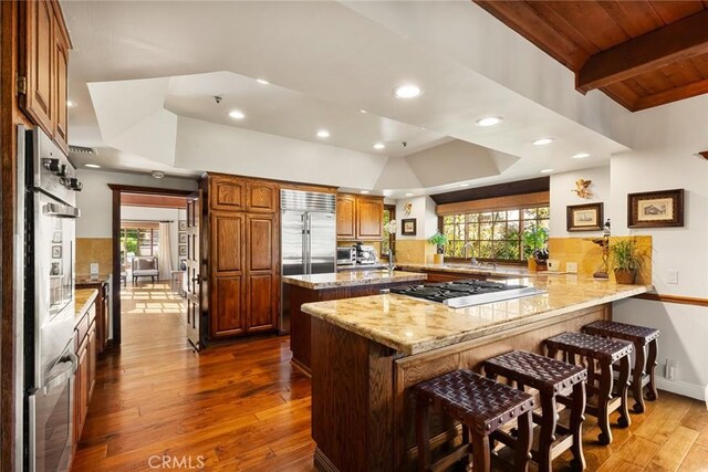 9 Maverick Ln, Bell Canyon, CA 91307 - kitchen with stainless steel appliances, a peninsula, a kitchen bar, dark wood-type flooring, and light stone countertops