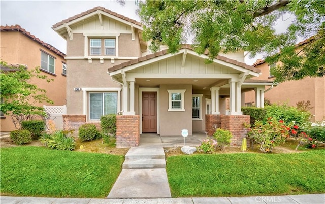 craftsman house with a front yard, stucco siding, and a tiled roof