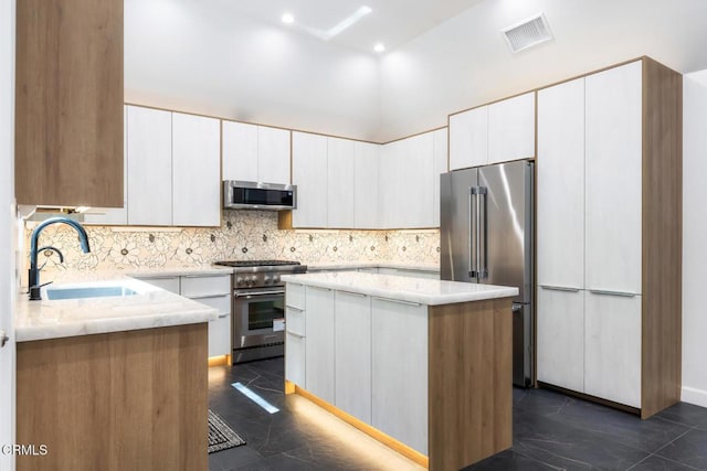 kitchen with high end appliances, a sink, a kitchen island, decorative backsplash, and light stone countertops