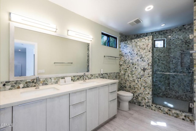 full bath with a stall shower, toilet, double vanity, tile walls, and recessed lighting