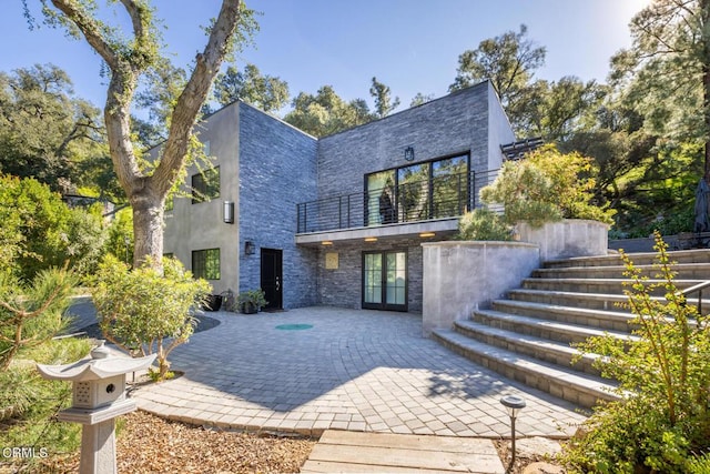 view of front facade featuring french doors, a patio area, a balcony, and stone siding