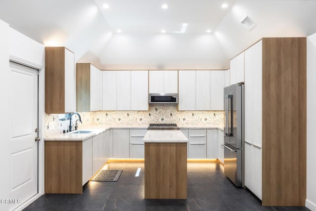 kitchen featuring appliances with stainless steel finishes, a sink, a kitchen island, light countertops, and backsplash