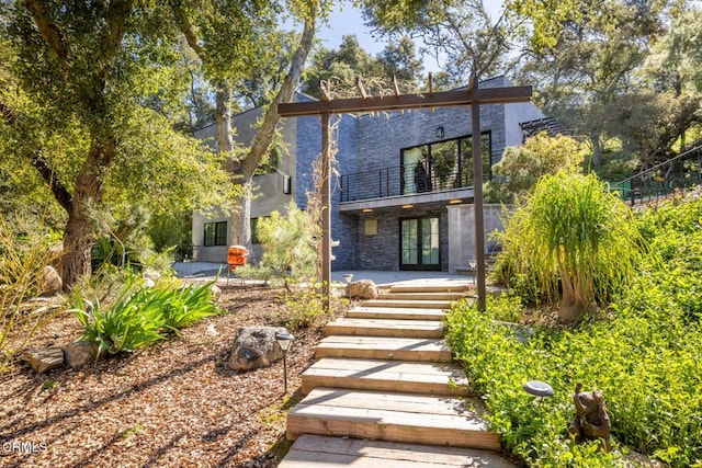 rear view of property featuring a balcony, french doors, stucco siding, stone siding, and a patio