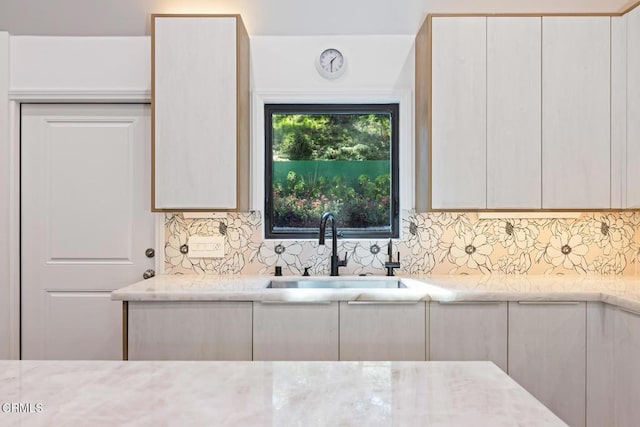 kitchen featuring a sink, backsplash, and light stone countertops