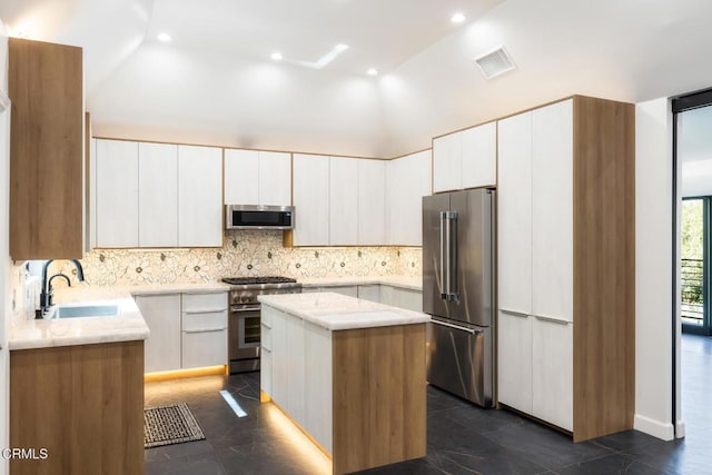 kitchen featuring premium appliances, a sink, a kitchen island, backsplash, and white cabinets