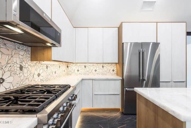kitchen with premium appliances, dark marble finish flooring, backsplash, white cabinets, and light stone countertops