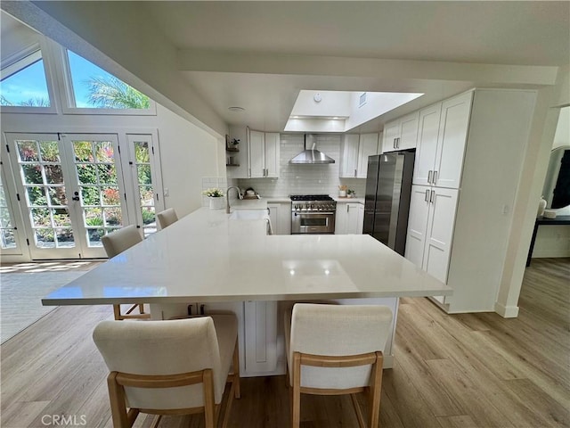 29521 Via, San Sebastian, Laguna Niguel, CA 92677 - kitchen with wall chimney exhaust hood, appliances with stainless steel finishes, tasteful backsplash, a peninsula, and light wood finished floors