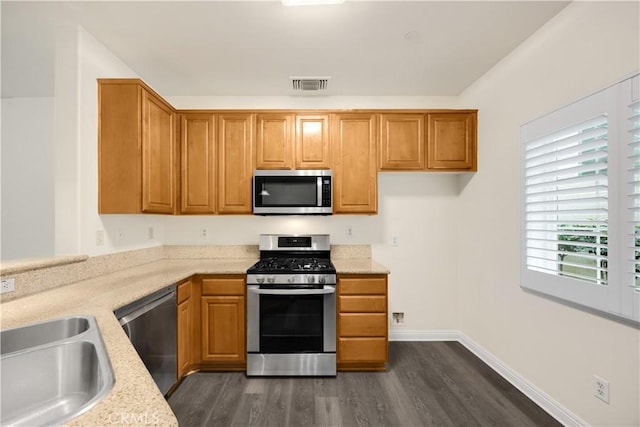 kitchen featuring stainless steel appliances, a sink, dark wood-type flooring, light stone countertops, and brown cabinetry