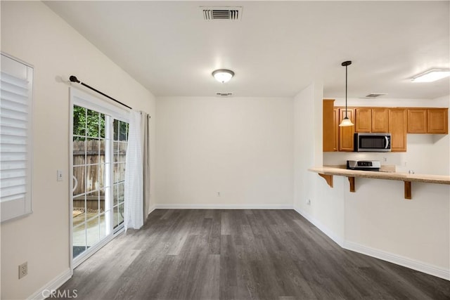 kitchen featuring stainless steel microwave, dark wood-style floors, brown cabinets, light countertops, and a breakfast bar