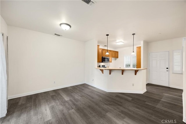 kitchen featuring stainless steel microwave, dark wood-style flooring, a breakfast bar area, and brown cabinets