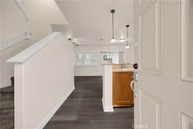 corridor featuring dark wood-style flooring, a sink, stairs, and baseboards