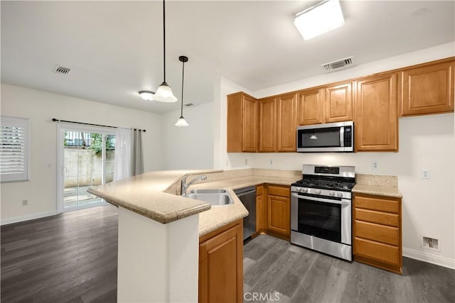 kitchen featuring appliances with stainless steel finishes, a sink, dark wood-style floors, a peninsula, and brown cabinetry